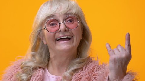 Positive granny showing rock n roll hand sign on bright background, feeling cool