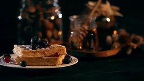 selective focus of sugar powder sifting on Belgian waffles with berries on black background