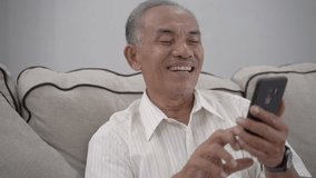 asian senior old man using smartphone while relaxing in livingroom at home