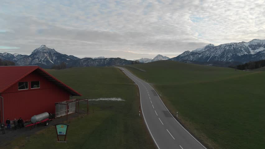 
A view from the top of the spring Austrian meadow and a view of the road through the meadows leading through the gorge to the Alpine mountains, the setting sun in the mountains, Austria Tyrol.