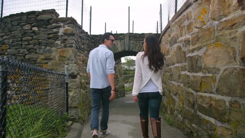 Couple Walks Under Old Rock Bridge on Coast