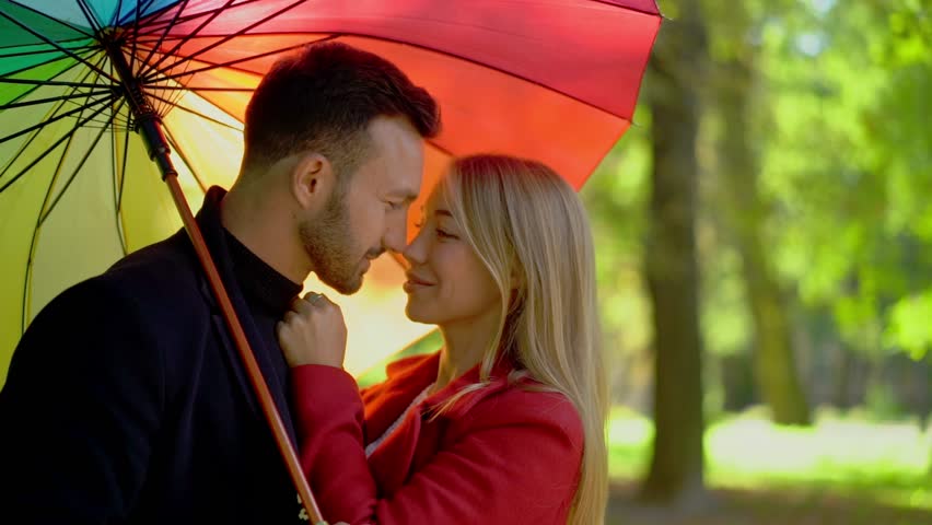 Couple In love Kissing Under Rainbow Umbrella. Having Date In Park.Lookinh Happy. Date In Nature Concept.