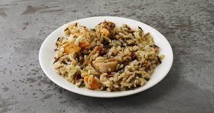 Video of taking a forkful of chicken with pecans and wild rice on a white plate atop a gray table illuminated with natural lighting.
