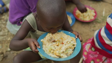 Rubuguri, Uganda - January, 2018: African child holding a plate full of food and eating.