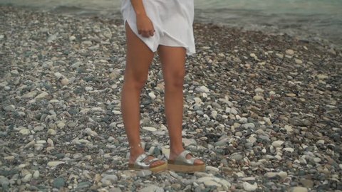 Young blond woman in white shirt standing at the beach looking far close up. Lonely girl spends time near the sea. Leisure of young lady. Camera moves up