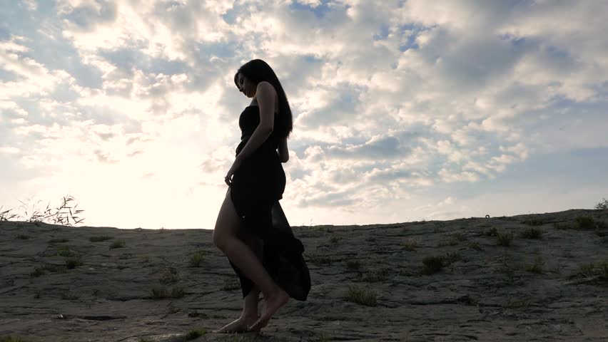 Sensual pretty young woman wearing long dress walking on the rocks