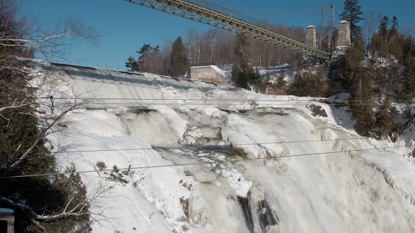 Scenic view of Montmorency falls in Quebec province in Canada. Depressive beautiful winter look of frozen waterfall and bridge in Quebec city
