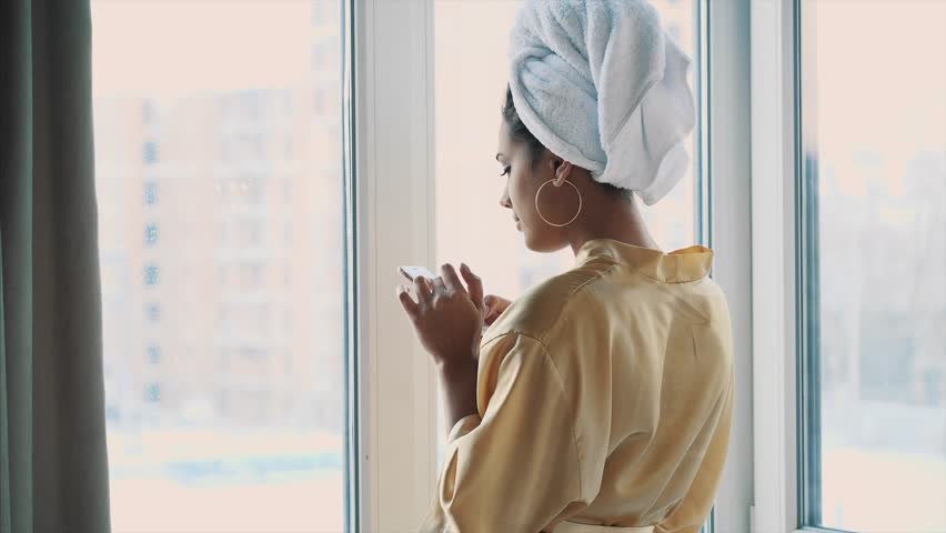 a young woman standing by the window, enjoying the window, looking at the phone.
