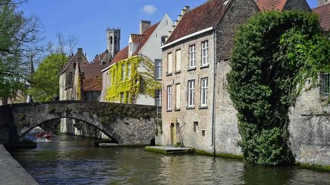 Bruges, Belgium - May 4, 2016. Belfry, old bridge over canal and tourists during sightseeing boat trip on the Groenerei, Bruges / Brugge, West Flanders, Belgium