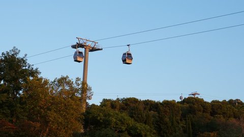 BARCELONA, SPAIN - AUGUST 18, 2018: Cabins of Teleferic de Montjuic cable car move by tower, view from ground level. Green area down under aerial lift ropes. Transportation system to top of Montjuc