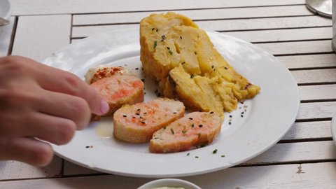 Spanish snacks, Tortilla (Potato Omelet) and sliced oiled baguette on small plate. Typical tapas or starters served at Barcelona cafe, closeup shot. Woman hand pick up one piece of bread