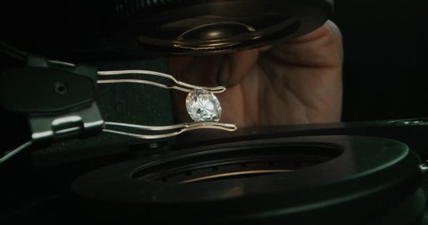 Slow motion macro close up of experienced goldsmith controlling a quality of diamond stone, selected for making jewels in workshop. Shot in 8K. Concept of jewelry,luxury,goldsmith,diamonds, brilliance