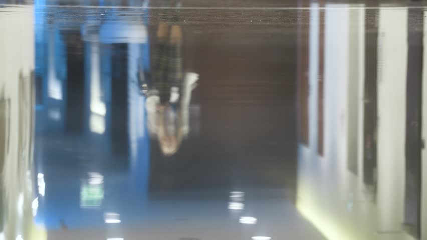 Reflection from the floor of people walking in different directions. People walk down the hall and open doors. Image is blurry.