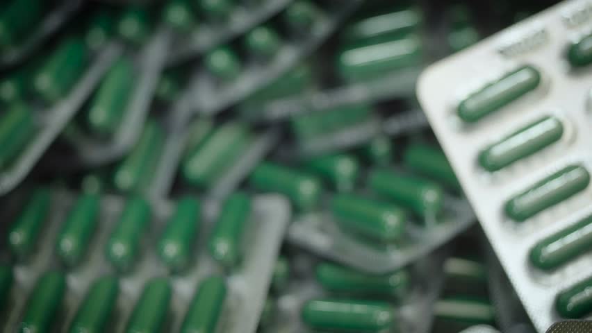 Falling green capsule pills in blister pack. Drug manufacturing, macro