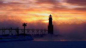 Foggy, steaming Winter sunrise time lapse of Algoma, Wisconsin lighthouse and steaming Lake Michigan waters with dramatic sky.