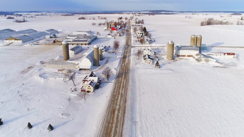 Scenic country road through snow covered rural community in Wisconsin in Winter, aerial flyover.