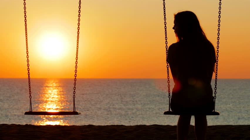 Back view silhouette of a sad girl at sunset missing her partner on a swing on the beach Royalty-Free Stock Footage #1023868432