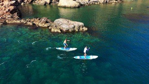 Porto Rafti, Athens / Greece - February 10 2019: Aerial drone video of 2 men in a paddle surf board known as Sup surfing in turquoise clear waters