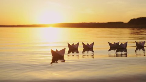 Many nice homemade paper boats floating in the river with a beautiful sunset background. Ships made from paper swimming on the water surface in the evening