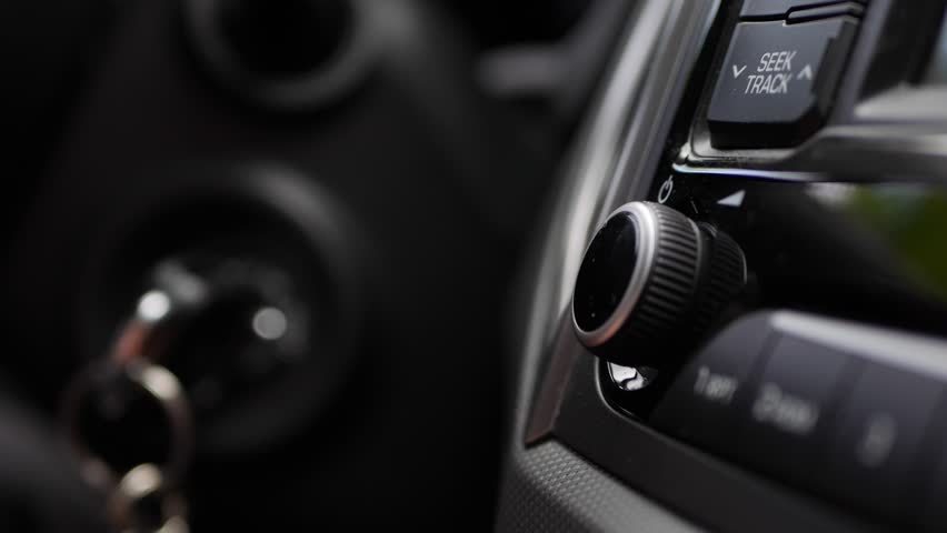 Male hand with a wedding ring turning the volume of the radio inside car on travel day commuting in big city listening to the music on highway. Volume level adjusting on car audio system. Closeup. 4k | Shutterstock HD Video #1023874327