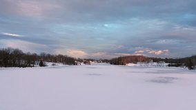 Aerial footage flying fast and low then rising up above a frozen lake towards a small village lit by the golden light of sunset