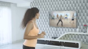 Attractive fitness woman doing workout while watching sport training on TV in living room at home. Shot in 4k resolution