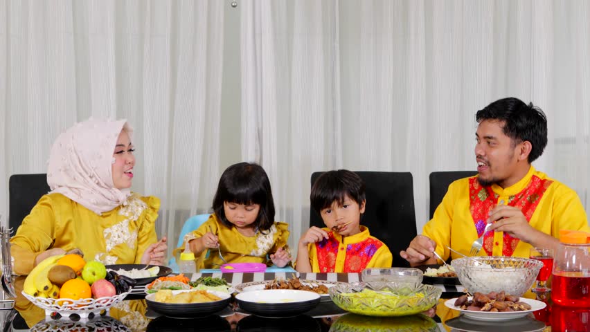 Attractive muslim family with two children having dinner on the table in the living room at home. Shot in 4k resolution
