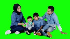 Happy family using a mobile phone while sitting on the floor in studio. Shot in 4k resolution with green screen background