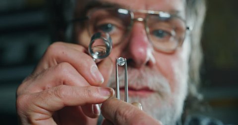 Slow motion macro close up of experienced goldsmith controlling a quality of diamond stone, selected for making jewels in workshop.Shot in 8K. Concept of jewelry,luxury,goldsmith, diamonds,brilliance.