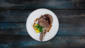 Rib-eye steak with corn rotating on a white plate. Top view on a wooden background