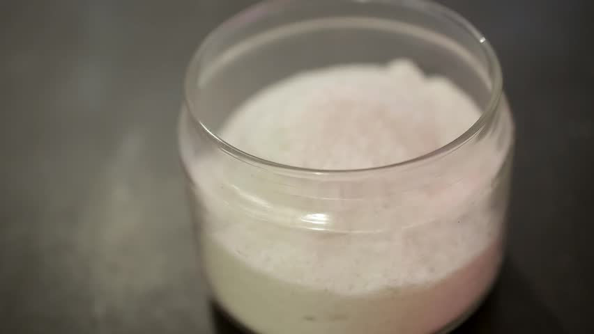 female hand covers the transparent jar of salt, which stands on a black table