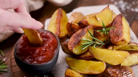Person eating rosemary baked potato wedges with ketchup. Unhealthy eating footage