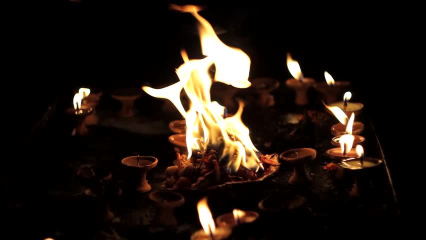 Diwali holiday. a plate with burning flowers in the background of small burning candles in clay stands in the dark.