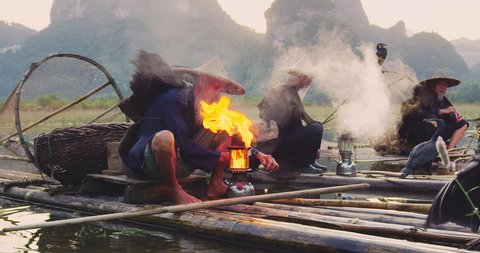 Cormorant fisherman lighting their lanterns on bamboo rafts at sunset on Li River, Xingping,  Guilin, Guangxi Province, China. Slow-motion, hand held, Red cinema camera. 