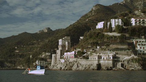 Shot of a fisherman boat out in the water with the mountains of the Amalfi Coast in the background. Wide shot on 8k helium RED camera.