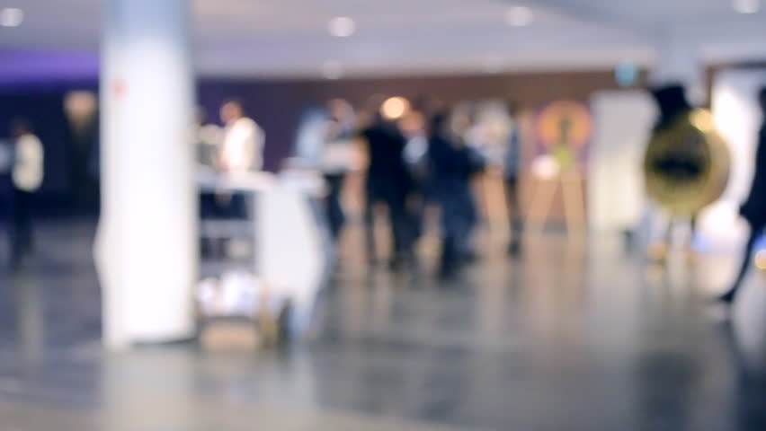 Blurred Background. People are standing behind the counter in the amount of white empty room. People stand behind the racks in a volume of white empty room. People communicate with each other
