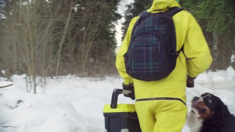 Woman ecologist with the dog walking along the road in winter forest. Steadicam shot, rear view