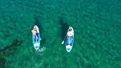 Porto Rafti, Athens / Greece - February 10 2019: Aerial drone video of 2 men in a paddle surf board known as Sup surfing in turquoise clear waters
