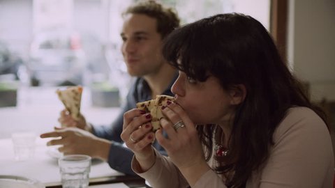 Group of friends eating slices of pizza and talking and laughing in a traditional Italian restaurant in Rome. Medium shot on 8k helium RED camera.