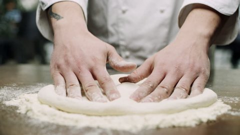 Italian pizza chef forming the dough on a floured surface and kneading it with his hands, in a traditional pizzeria kitchen. Close up shot on 8k helium RED camera.