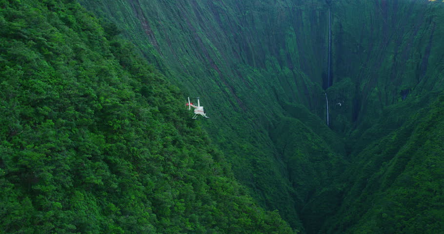 Aerial view of helicopter flying towards giant waterfall in amazing lush green valley, epic helicopter adventure, slow motion