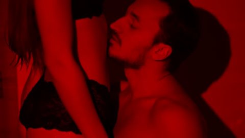 Passionate man kissing belly of woman close up in slow motion. Lovers have foreplay. Beautiful couple making love in private place. Shooting in bright red light.