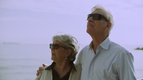 Elderly couple looking out at the buildings and the landscape of the Amalfi Coast from a dock by the ocean. Wide shot on 8k helium RED camera.