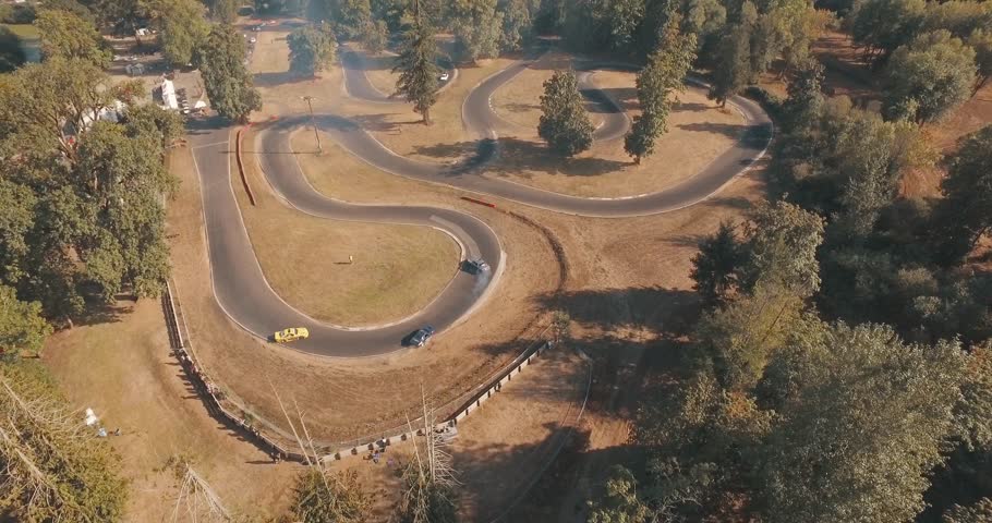 Wide Aerial Drone Tracking Shot of Race Cars Drifting Around Hair Pin Curves on a Race Track.