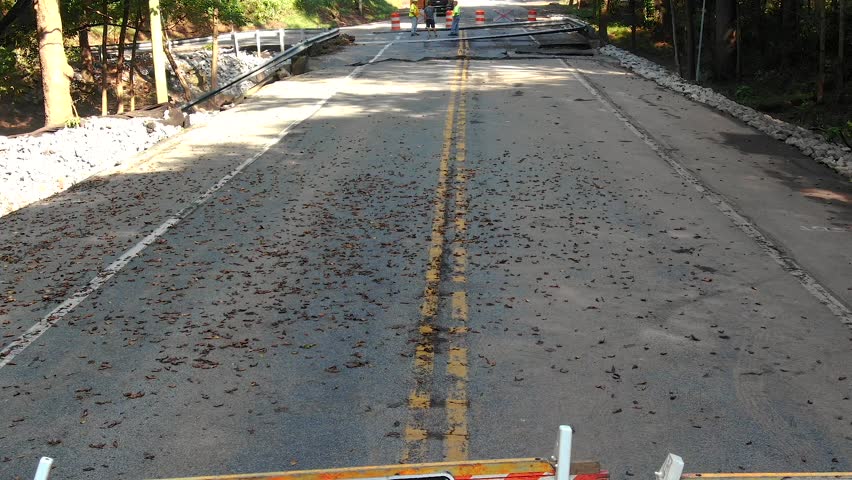 Washed out bridge across Hammer Creek in Lancaster County, Pennsylvania, damaged in floodwaters, road signs warning drivers, construction workers in background, aerial revealing shot