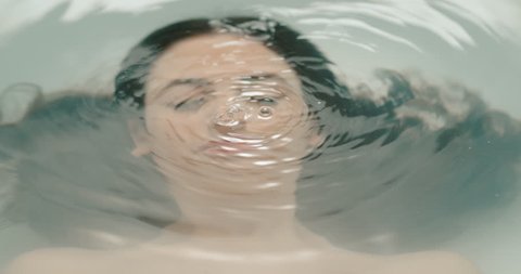 slow motion of a young woman in a bathtub drowning her face under water making bubble
