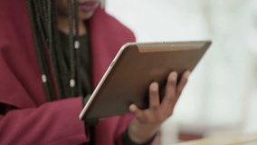Close up shot of Afro-American young girls hands in rose coat, sitting outside and typing on tablet. Communication lifestyle, wireless technology concept