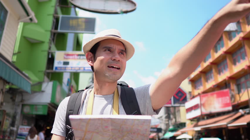 Asian tourist man looking for direction at the map while solo traveling in Khao San road Bangkok, Thailand