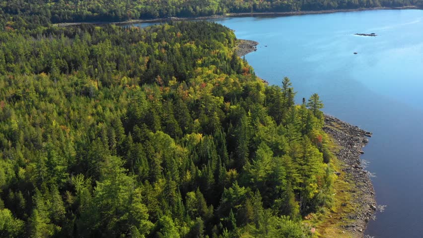 Early fall aerial footage of remote lake in northern Maine orbiting around a wooded rocky shoreline