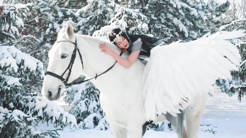 charming dark queen went for walk in fairy-tale creation, lady with black hair and silver tiara gently strokes white pegasus with love and tenderness, creative idea with horse and artificial wings